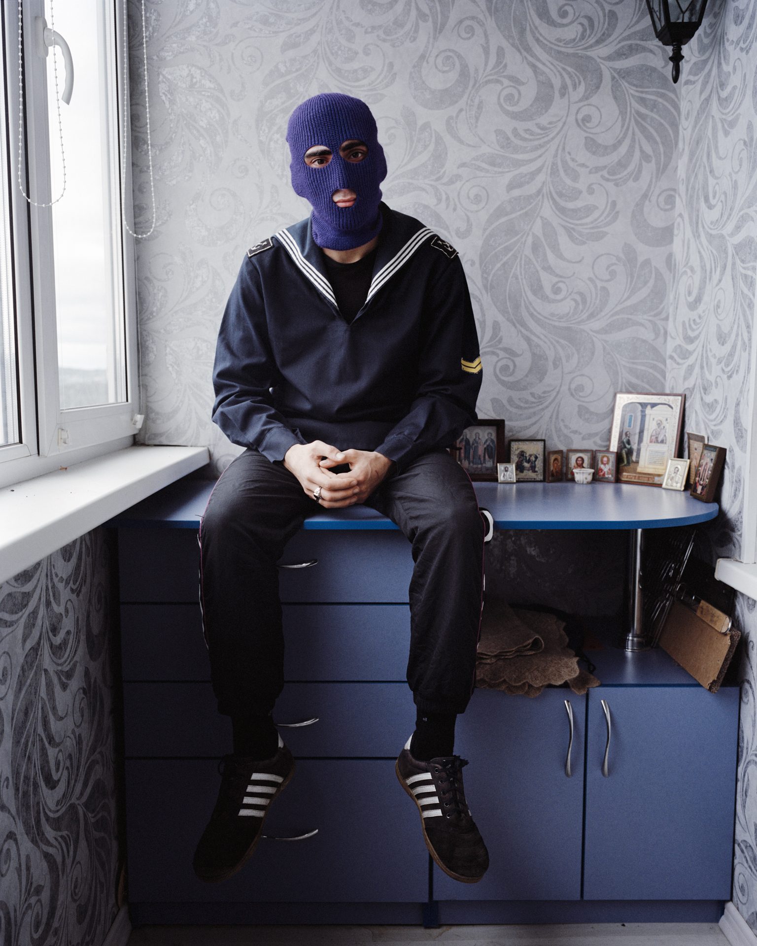 Conscript in a balaclava sitting by a kitchen window